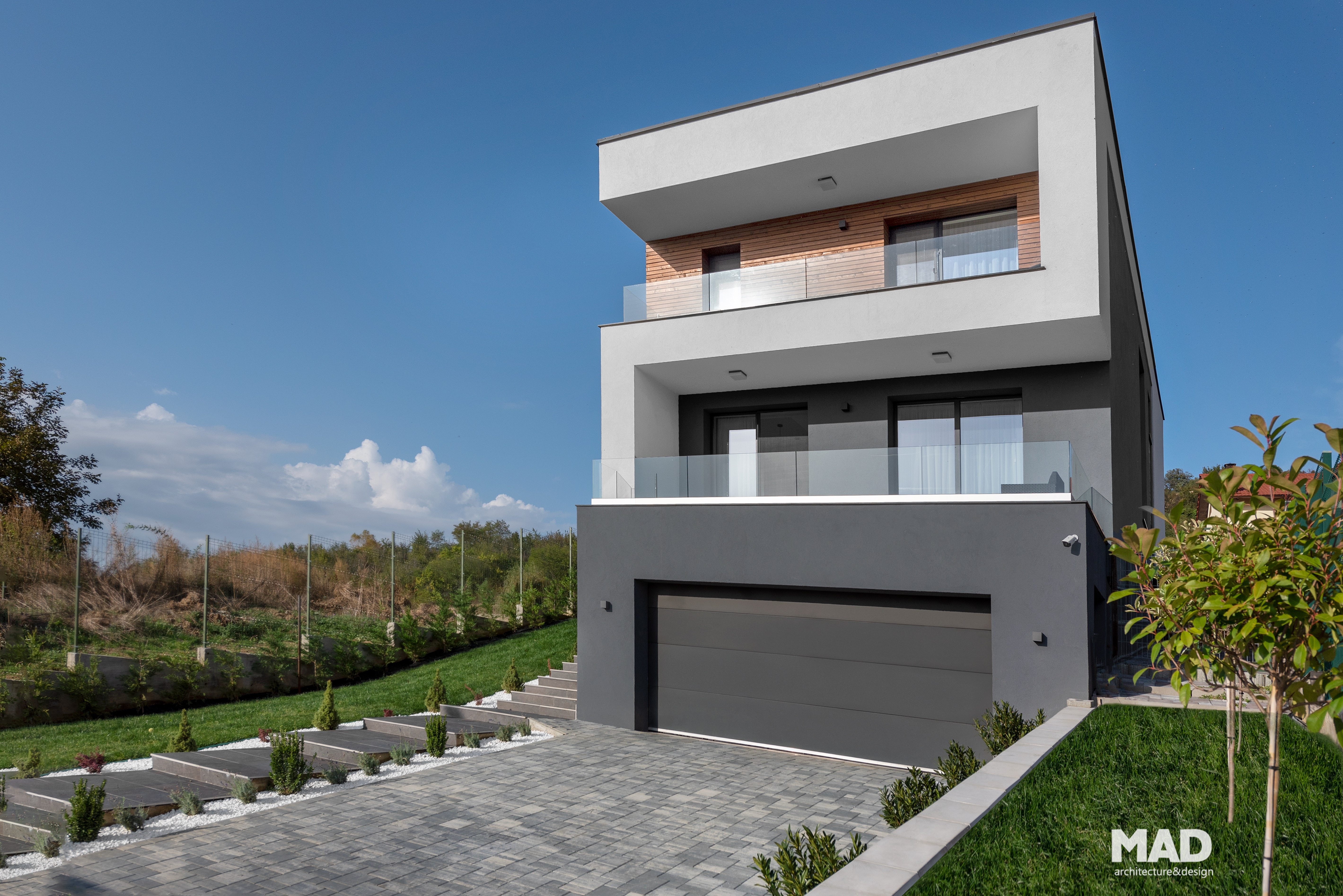 Casă contemporană cu volumetrie minimalistă și acoperiș terasă, realizată de MAD architecture&design, finisaje exterioare din lemn, ardezie și tencuială albă.