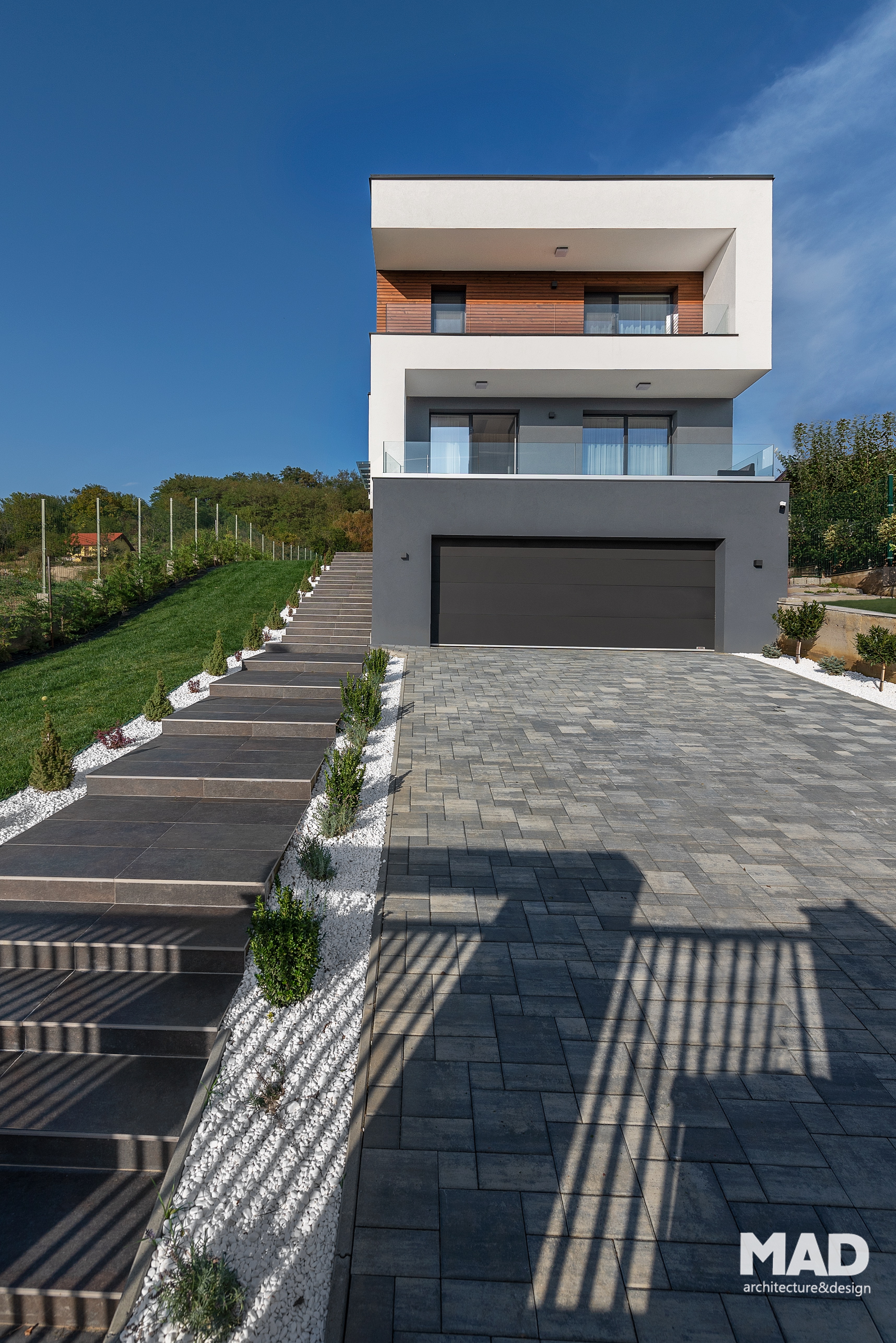Vedere frontală a unei case moderne, regim de înălțime D+P+E, proiect MAD architecture&design, fațadă din tencuială albă, gri antracit și inserții din lemn.