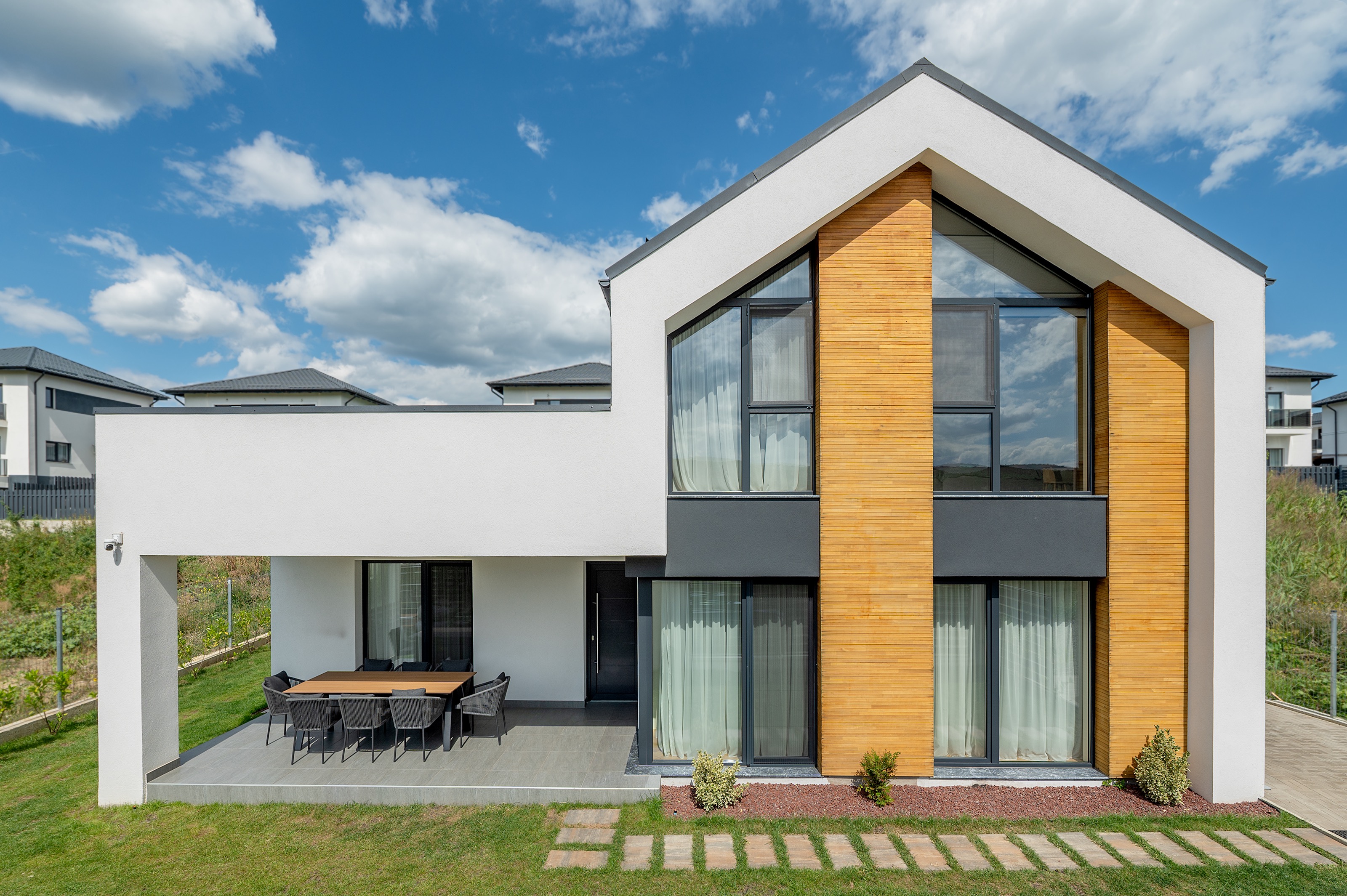 Fațada principală a casei moderne P+1 Casa U, proiect MAD architecture&design, arhitectură contemporană cu placaj de lemn, tencuială albă și gri antracit, geamuri ample pe verticală.