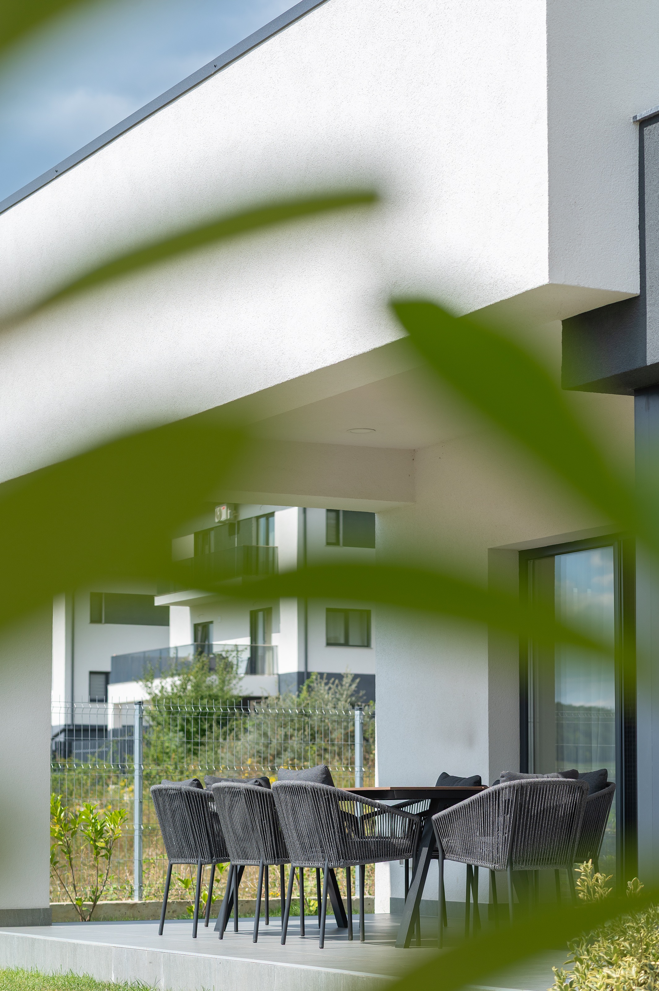 Terasă acoperită a casei moderne P+1 Casa U, proiect MAD architecture&design, spațiu exterior elegant cu mobilier de design, finisaje din tencuială albă și tonuri gri.