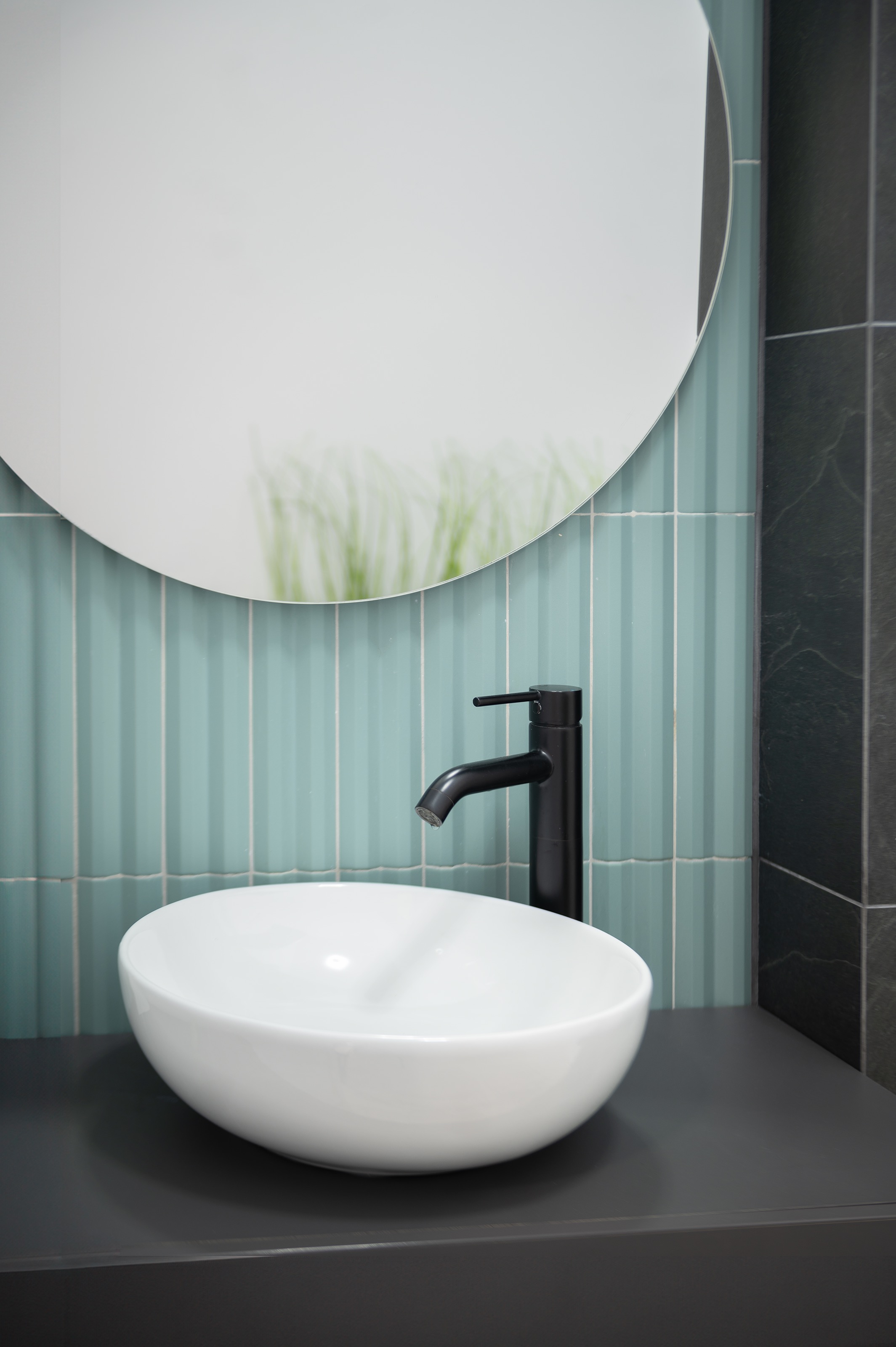 Design interior modern pentru grup sanitar în clinica stomatologică The Nest Cluj-Napoca, realizat de MAD architecture&design, cu lavoar alb pe blat gri, robinet negru mat și faianță verde menta pastel cu placute de gresie riflate, oglinda rotunda.