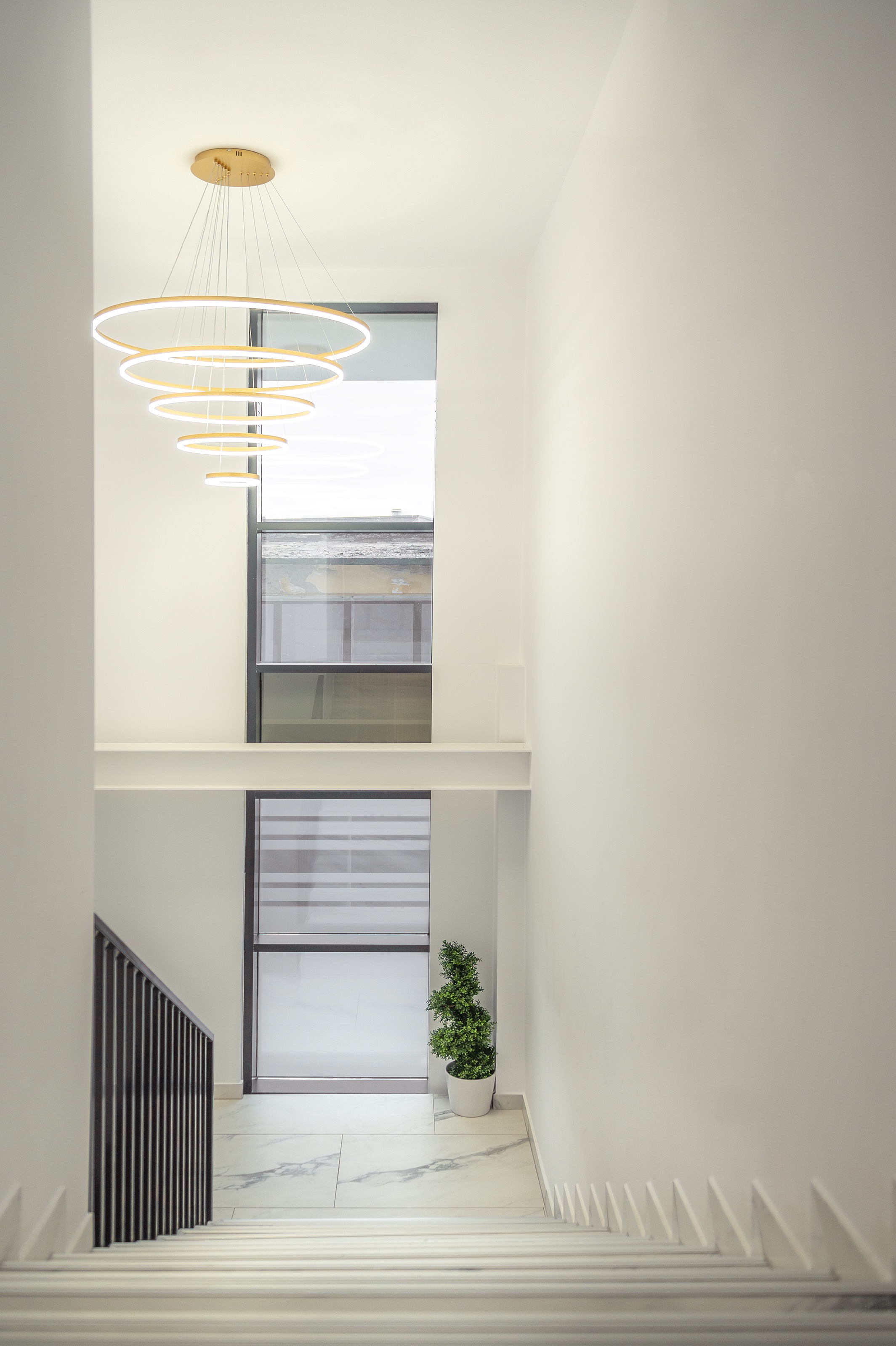 Corp de iluminat circular cu 5 cecruri led aurii, candelabru suspendat într-un spațiu minimalist alb, proiectat de MAD architecture&design pentru casa scării clinicii The Nest Cluj-Napoca.