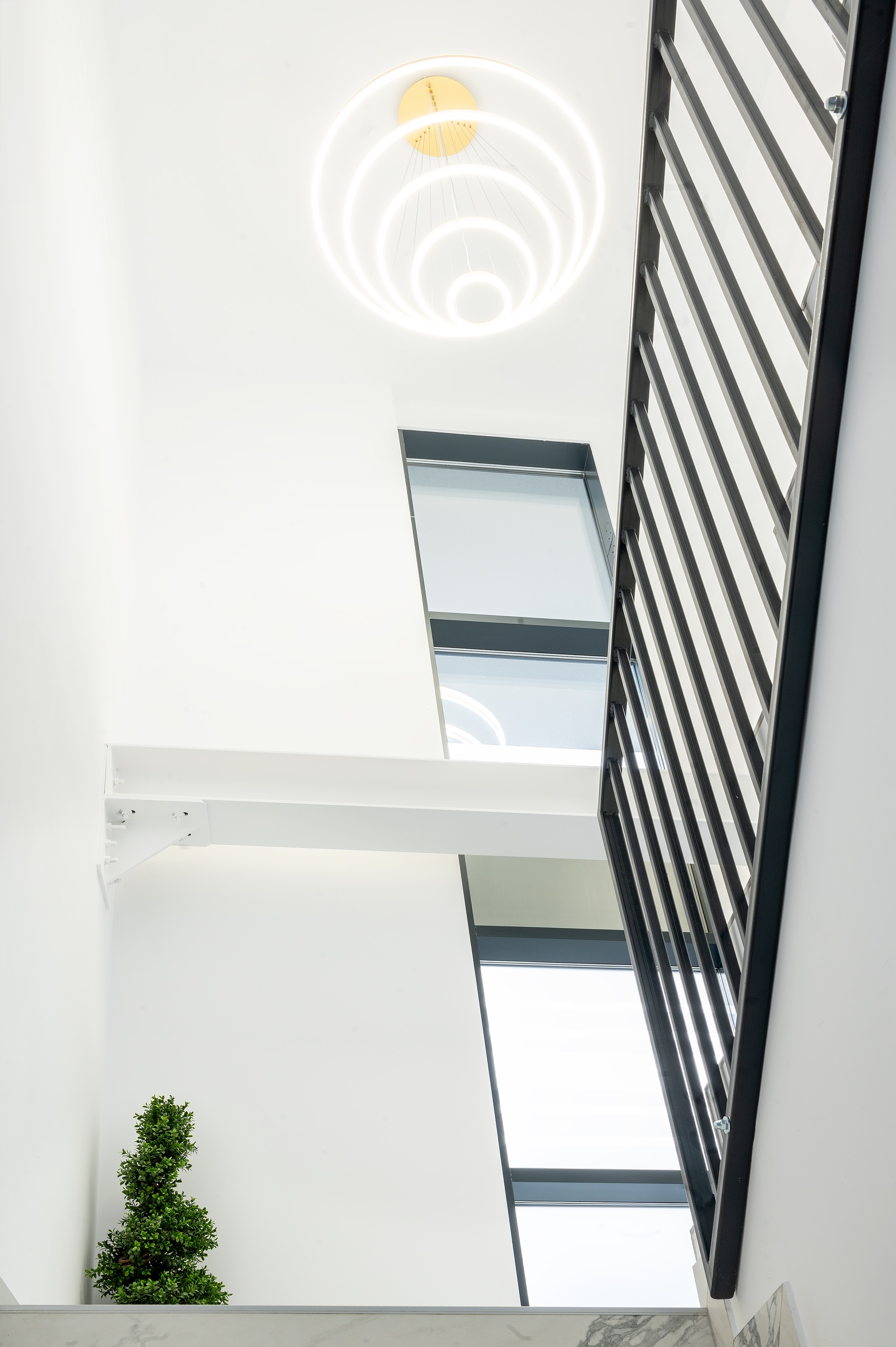 Casa scării luminoasă și modernă a clinicii The Nest Dental Clinic Cluj-Napoca, cu balustradă neagră metalică, trepte din marmură albă și plante decorative, design MAD architecture&design.