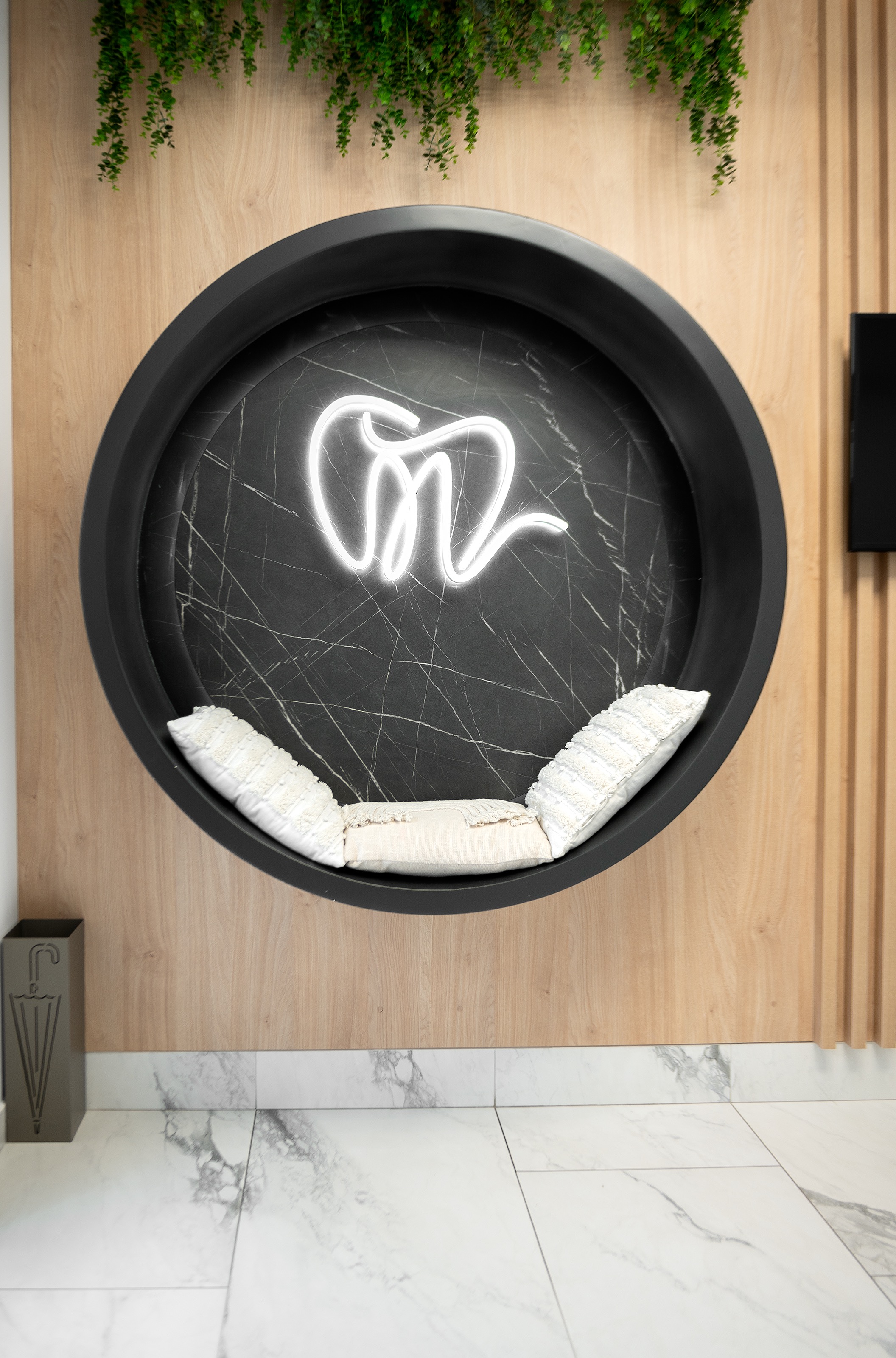 Colț foto cu design personalizat în The Nest Dental Clinic, creat de MAD architecture&design, având o nișă rotundă cu fundal de marmura neagră, logo cu led luminos și perete din lemn, decorat cu plante curgatoare.