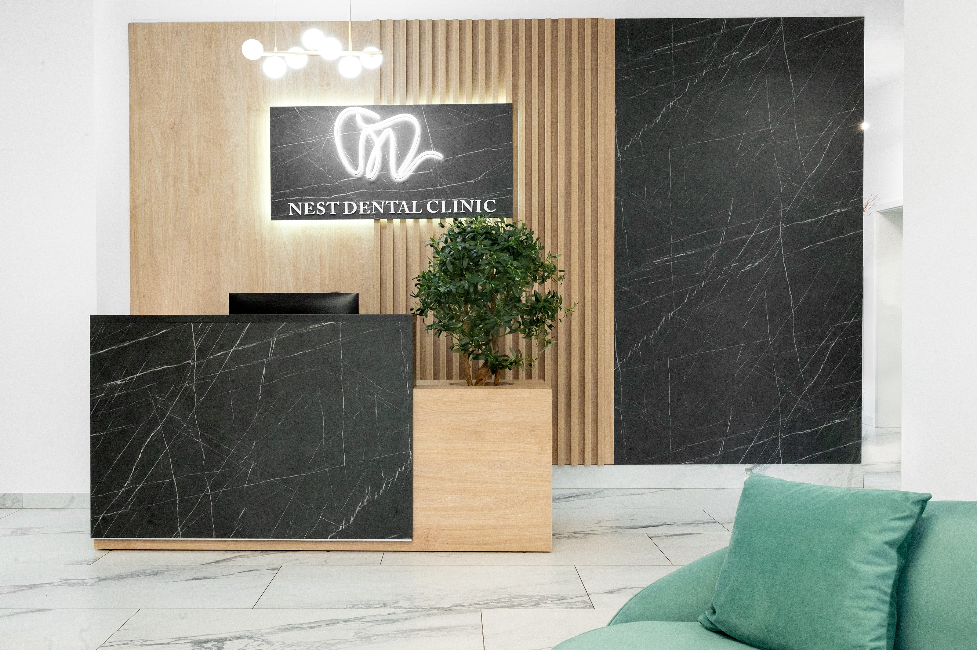 Recepția principală a clinicii The Nest Dental Clinic Cluj-Napoca, amenajată de MAD architecture&design, cu mobilier din lemn și marmura neagră, iluminare ambientală și copacel integrat in mobilierul de receptie.