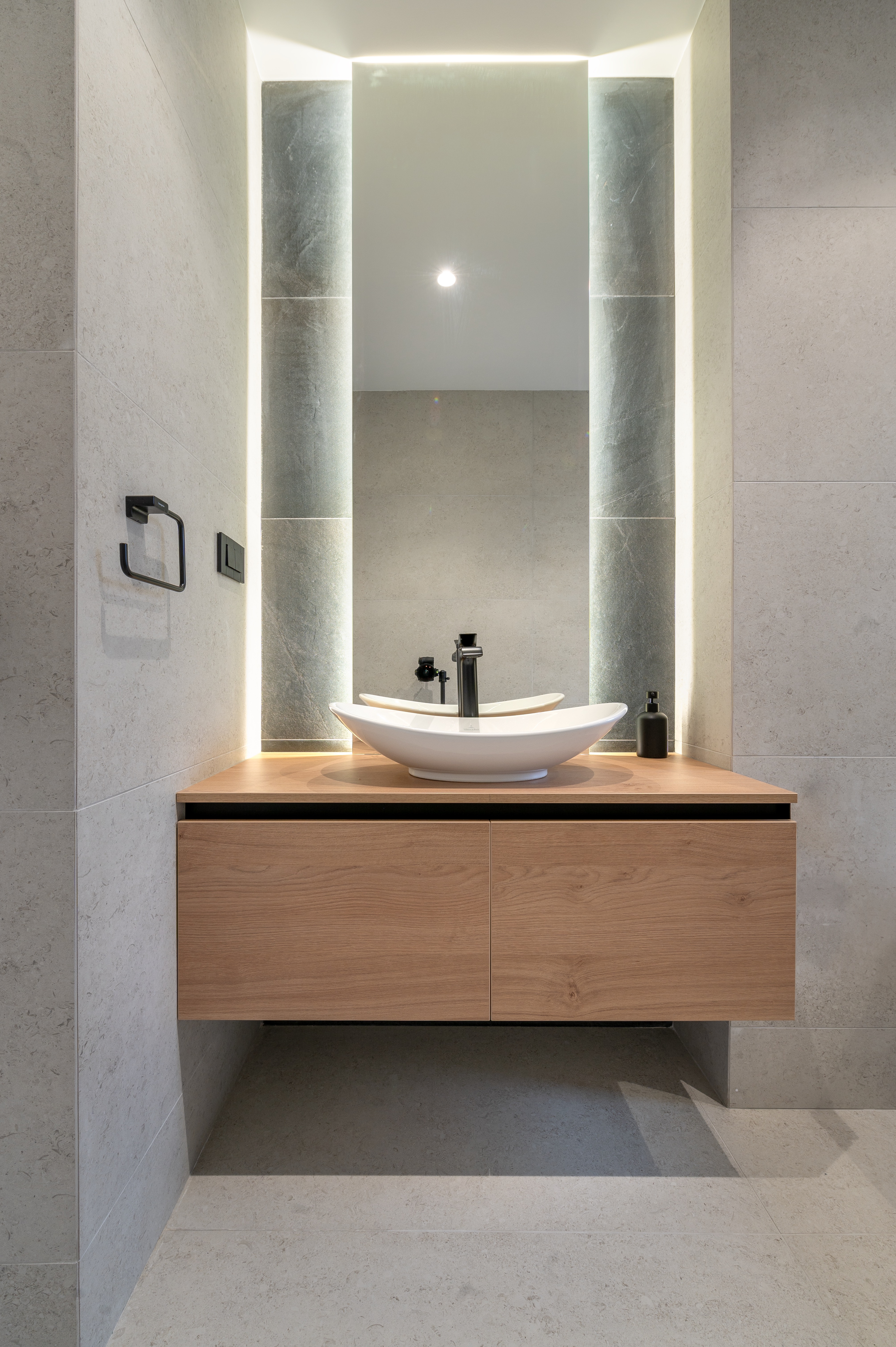 Design contemporan pentru baie de oaspeți, cu blat din lemn, lavoar alb tip bol, oglindă verticală luminată LED și detalii negre moderne – MAD architecture&design