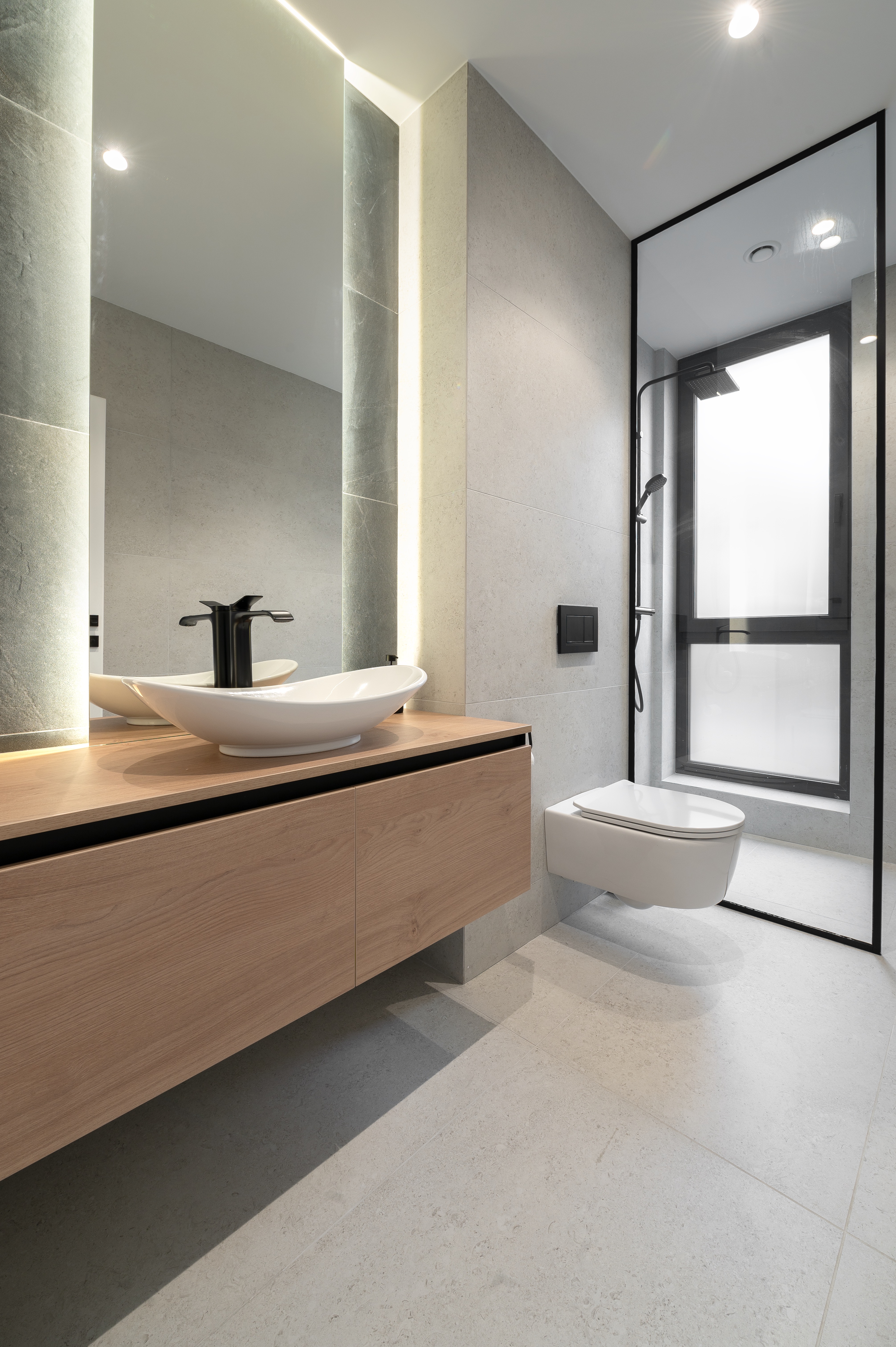 Baie pentru oaspeți în stil minimalist, cu mobilier suspendat din lemn natural, lavoar tip bol, paravan de duș din sticlă neagră și finisaje gri deschis – MAD architecture&design.
