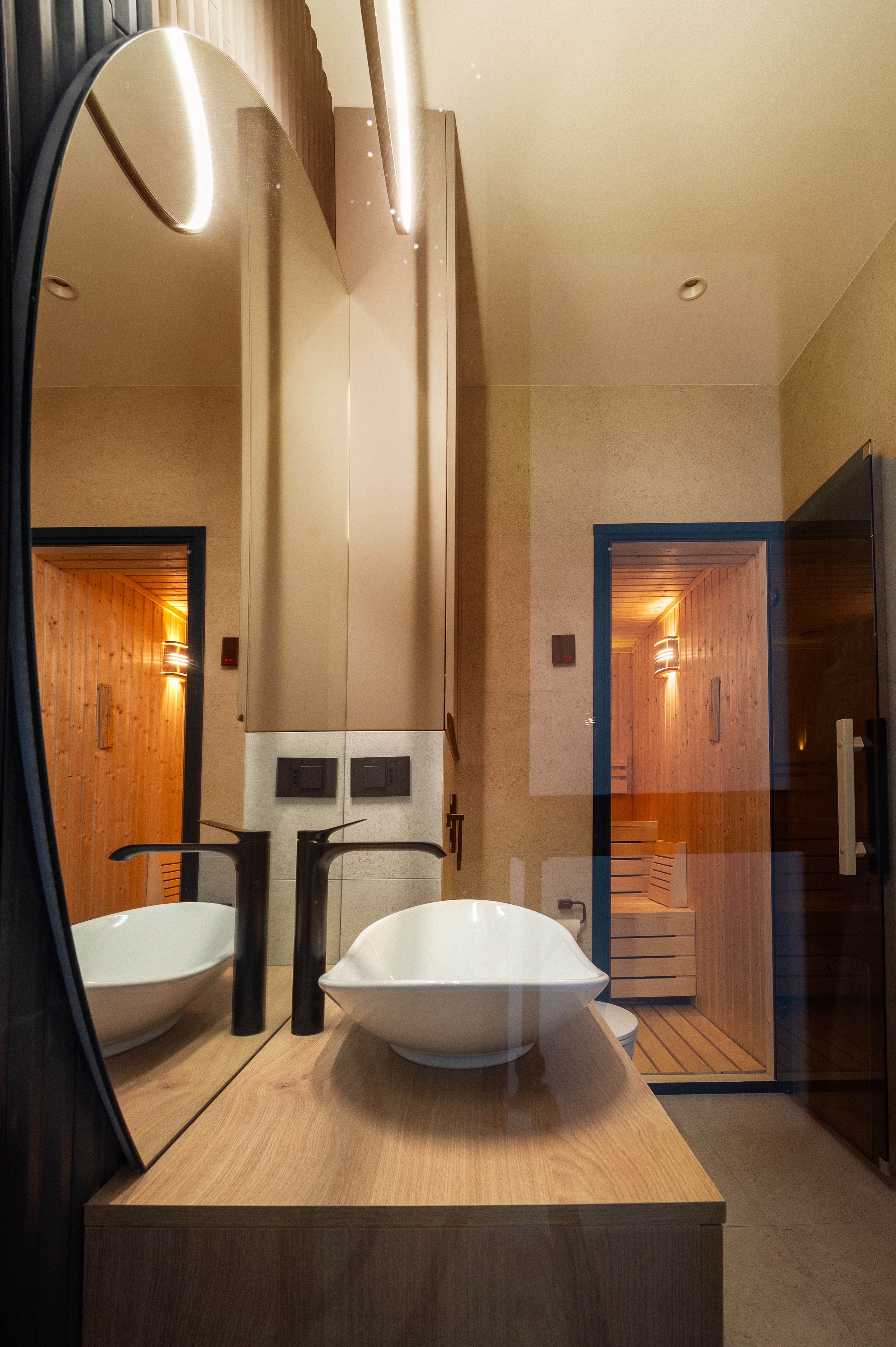 Baie contemporană cu finisaje bej deschis și zonă de saună din lemn natural iluminată ambiental – design MAD architecture&design.
