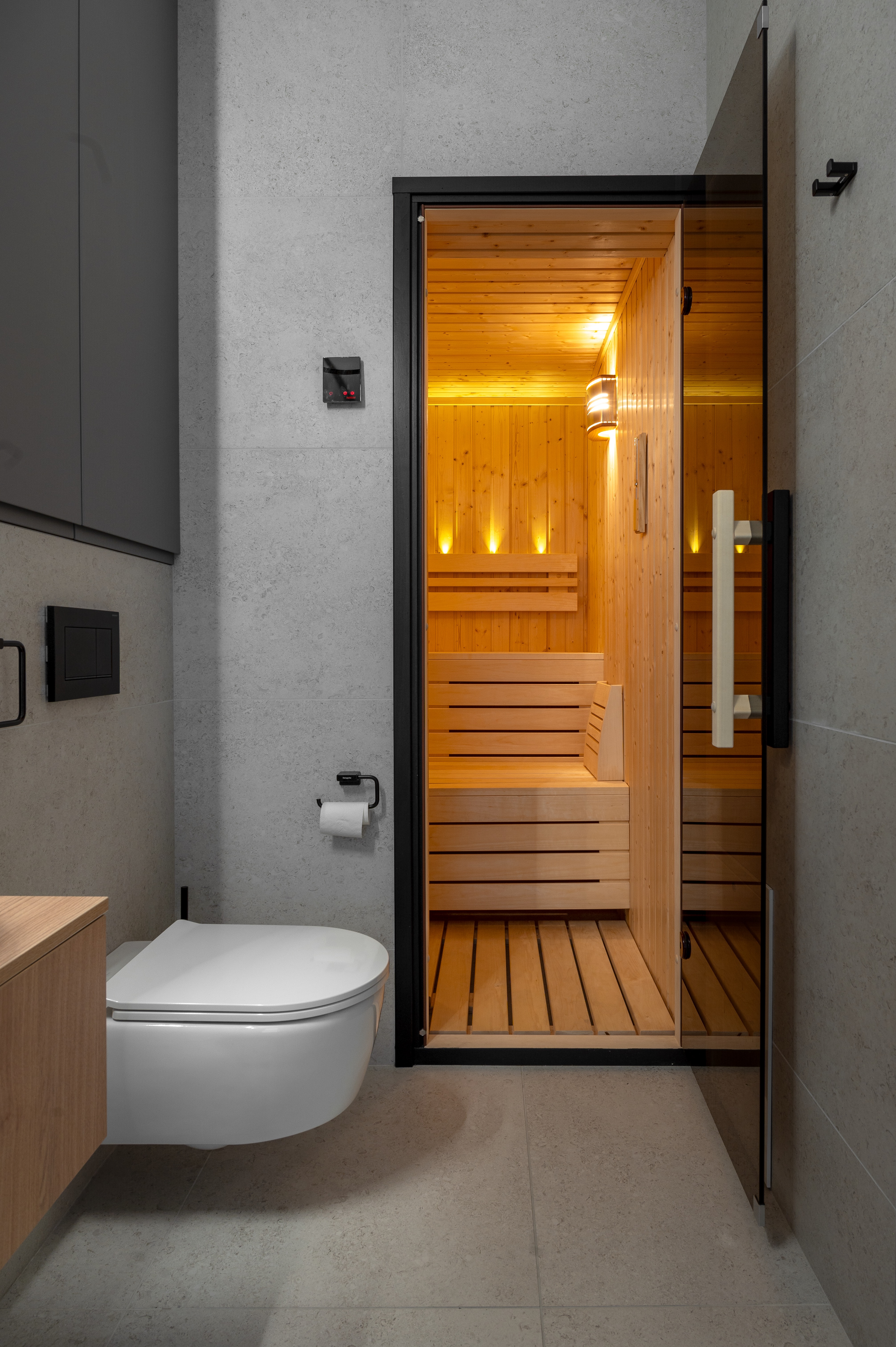 Baie modernă cu vas de toaletă suspendat și acces direct către sauna din lemn, într-un decor minimalist și elegant – MAD architecture&design.