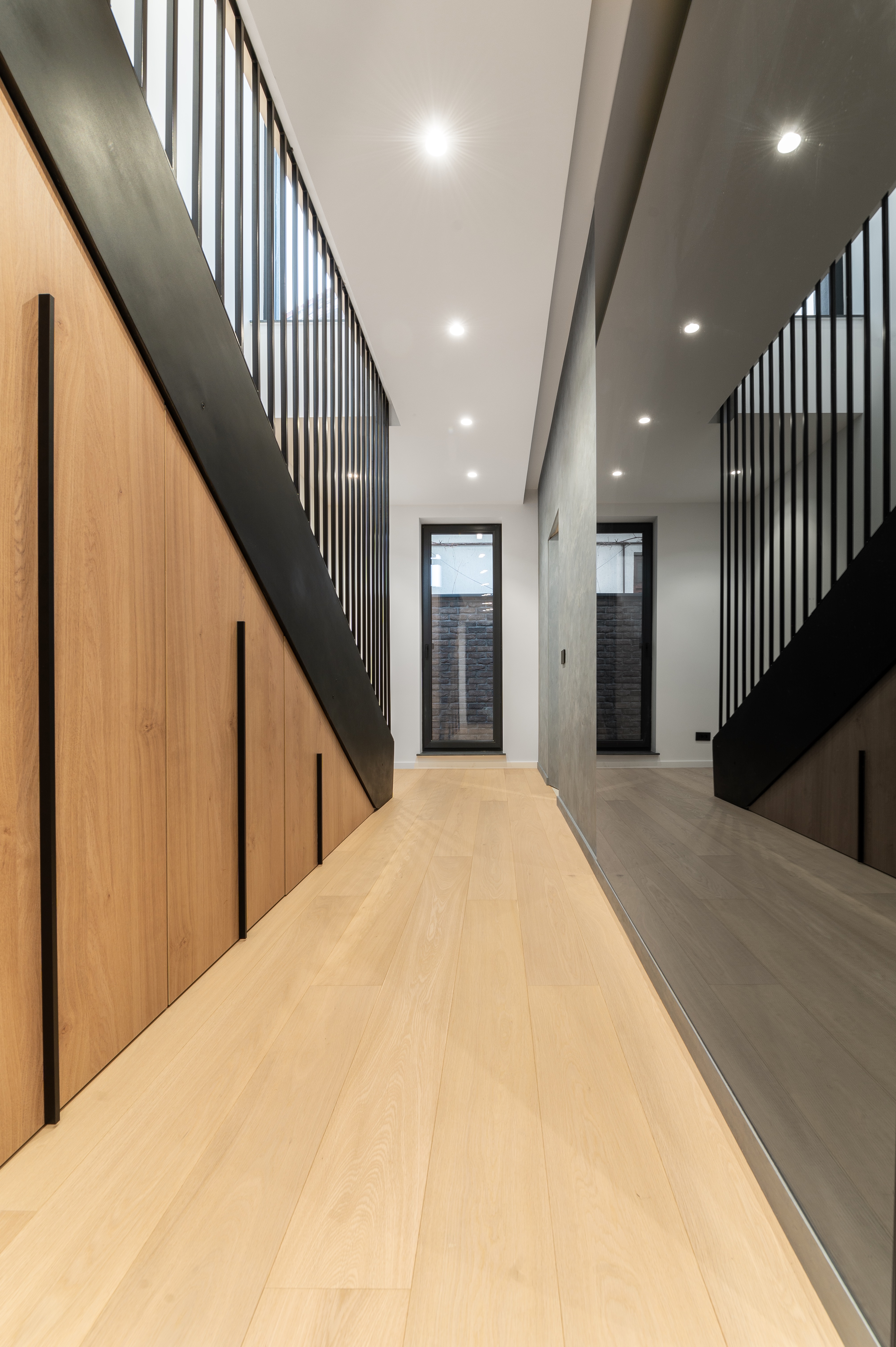 Spațiu de depozitare integrat sub casa scării, realizat din panouri de lemn cu detalii negre, într-un design minimalist – MAD architecture&design.