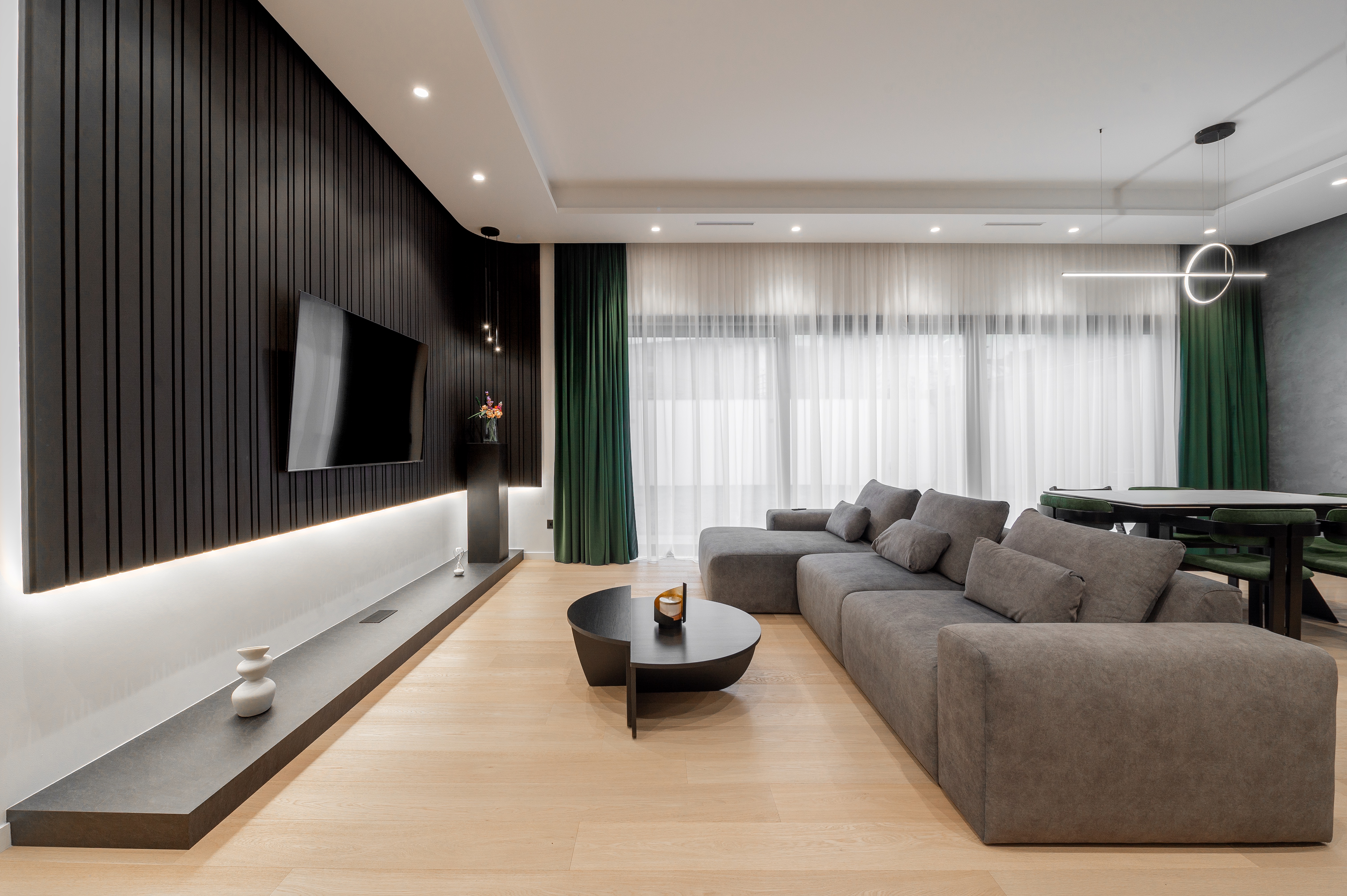 Living sofisticat, cu panou TV vertical negru, mobilier minimalist și pardoseală din lemn deschis, completate de iluminare LED subtilă – design MAD architecture&design.
