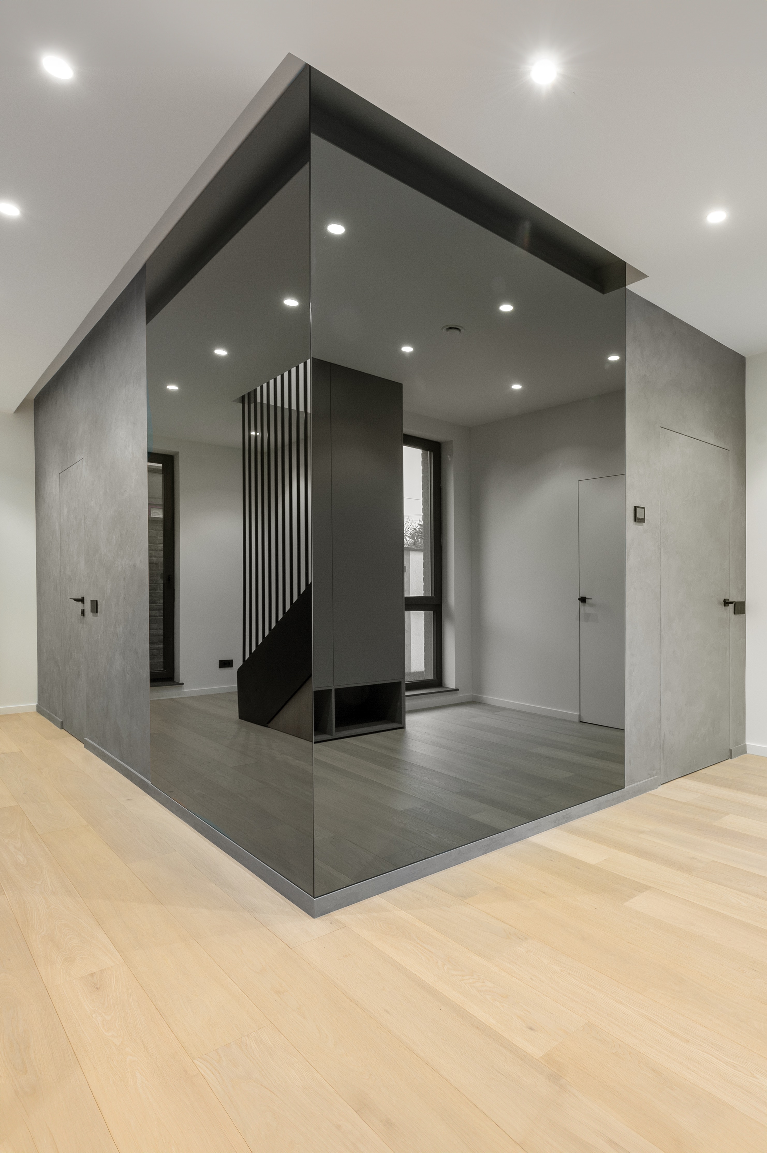 Hol contemporan cu finisaje gri texturate, pardoseală din lemn și pereți placați cu oglinzi fumurii ce amplifică spațiul – design MAD architecture&design.