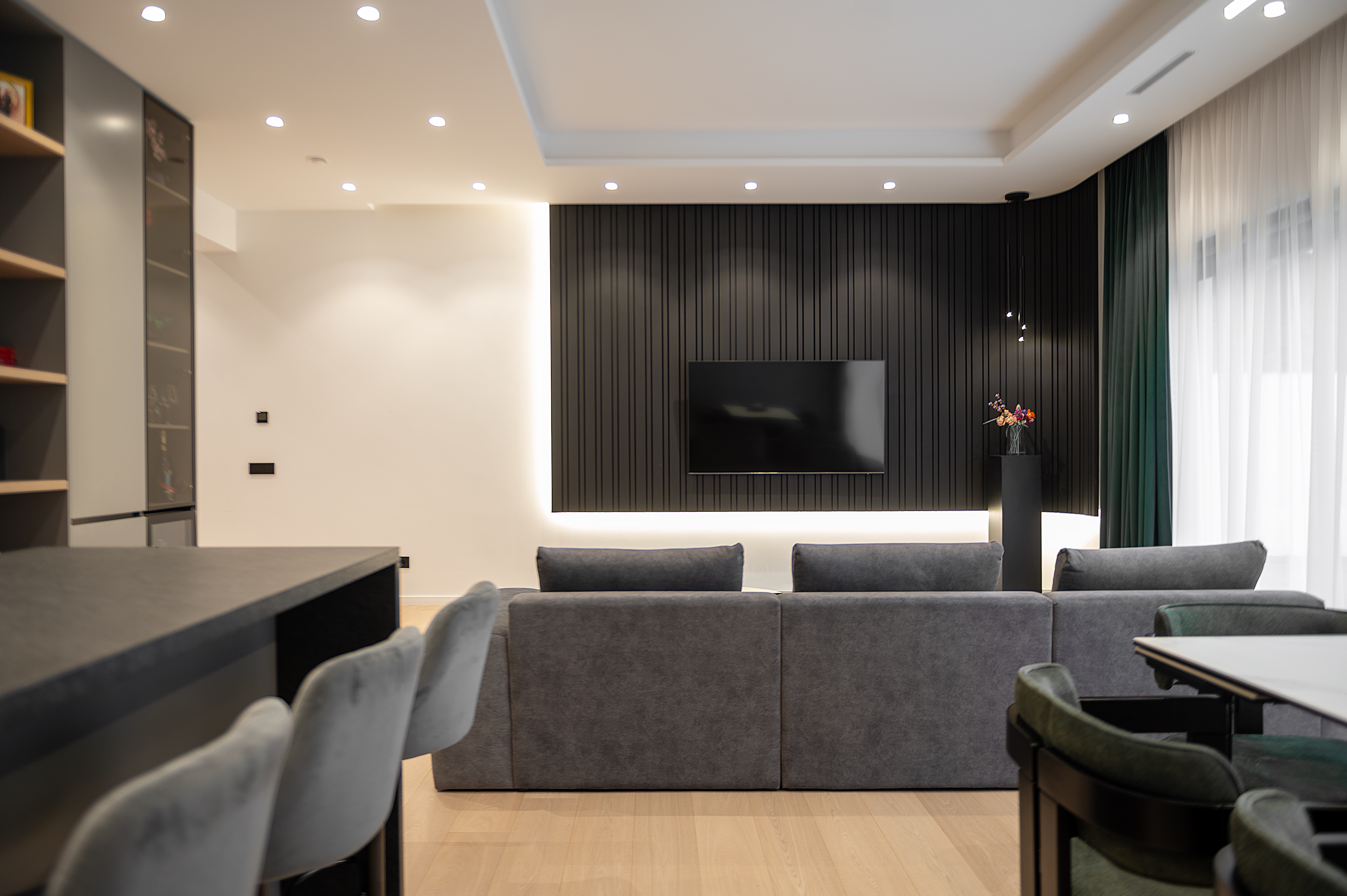 Living modern cu perete TV negru lamelar, canapea gri și accente de lumină caldă ce conturează atmosfera elegantă a spațiului – MAD architecture&design.